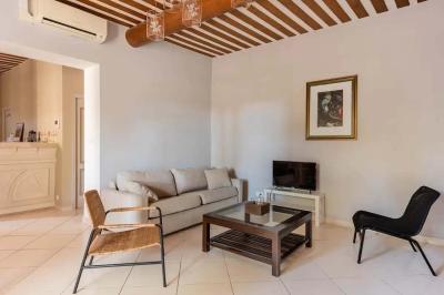 Salon avec canapé beige, fauteuils, table basse, télévision, cheminée en pierre et plafond avec poutres apparentes.