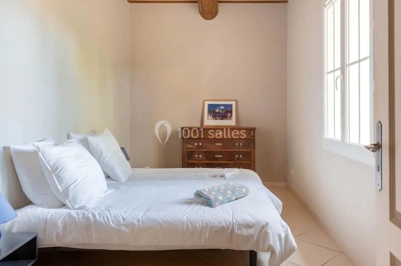 Chambre lumineuse avec deux lits simples, une commode en bois et une fenêtre laissant entrer la lumière naturelle.