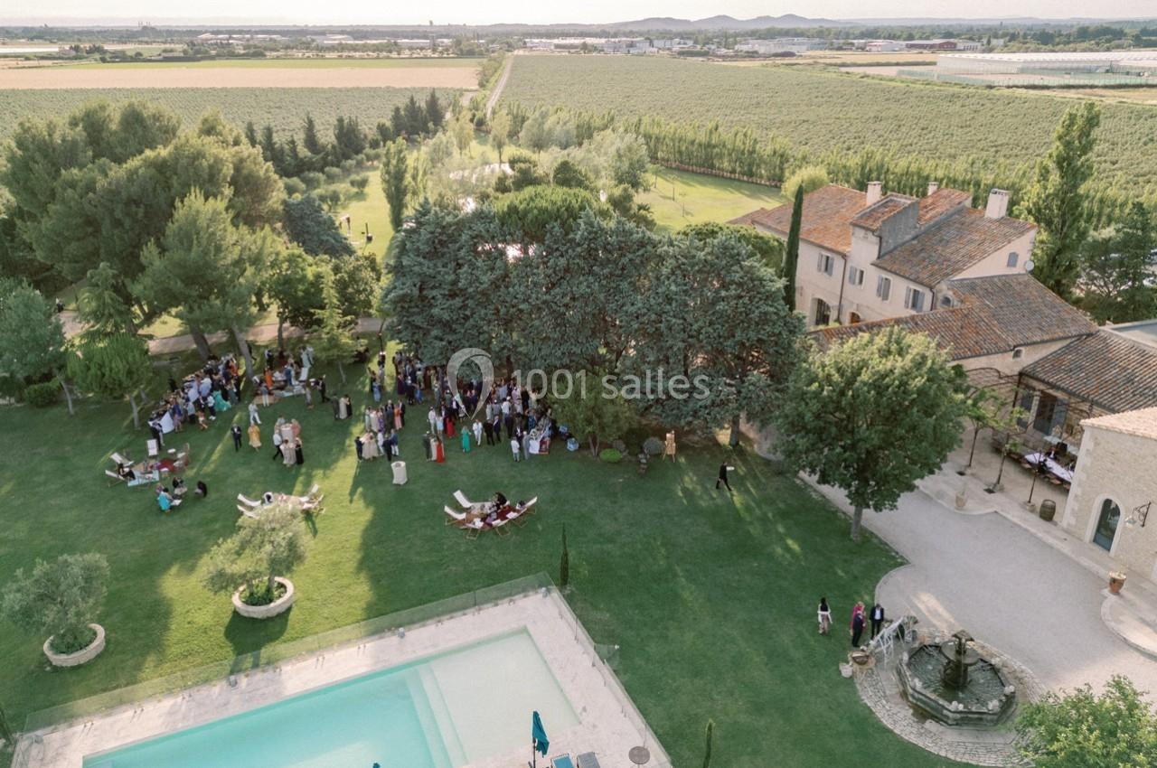 Vue aérienne d'un domaine avec piscine, jardins verdoyants, invités rassemblés et bâtiments en pierre.