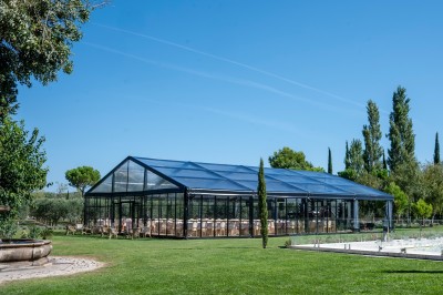 Tables dressées pour un dîner en plein air sous des guirlandes lumineuses, devant un bâtiment ancien au crépuscule.