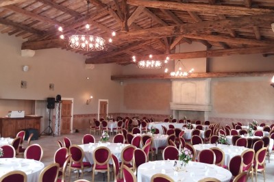 Tables dressées pour un dîner en plein air sous des guirlandes lumineuses, devant un bâtiment ancien au crépuscule.