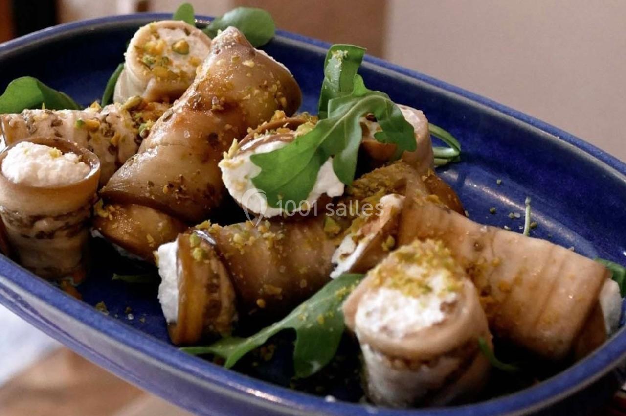 Roulés d'aubergines garnis de fromage frais, servis sur un lit de roquette et saupoudrés de pistaches.