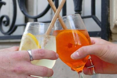 Deux verres de cocktails, l'un avec une tranche de citron, l'autre avec une tranche d'orange, tenus par deux mains.