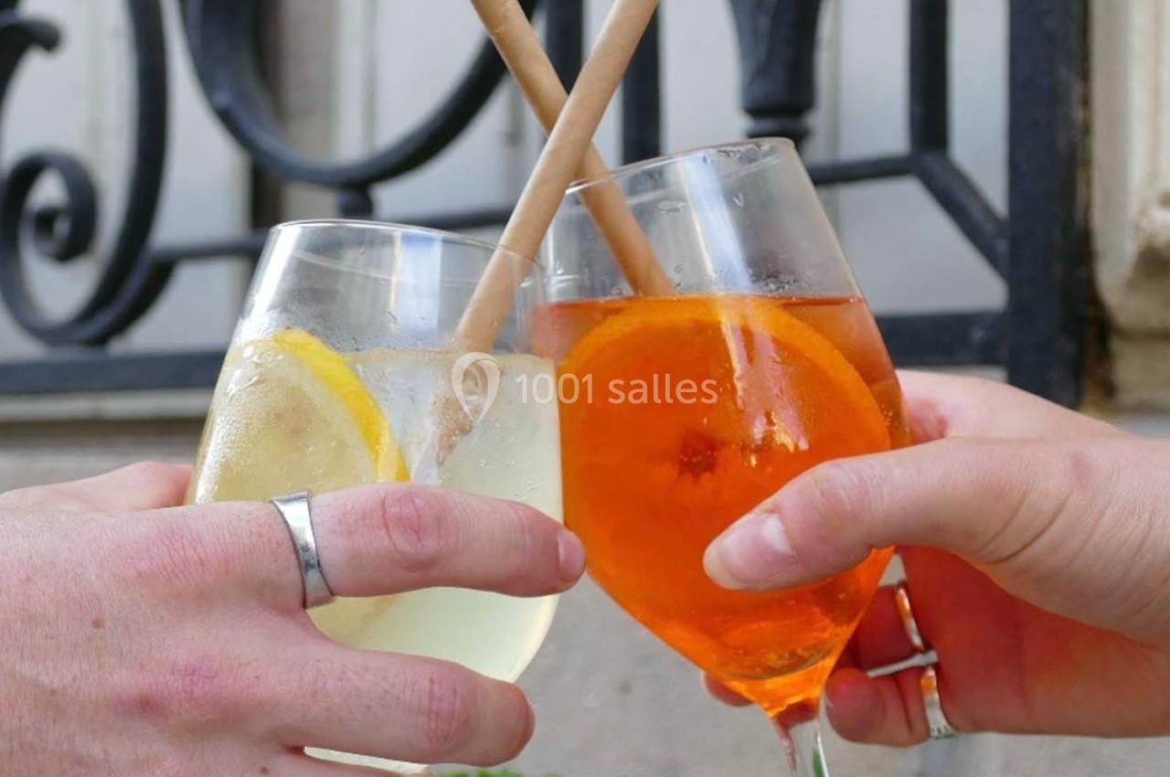 Deux verres de cocktails, l'un avec une tranche de citron, l'autre avec une tranche d'orange, tenus par deux mains.