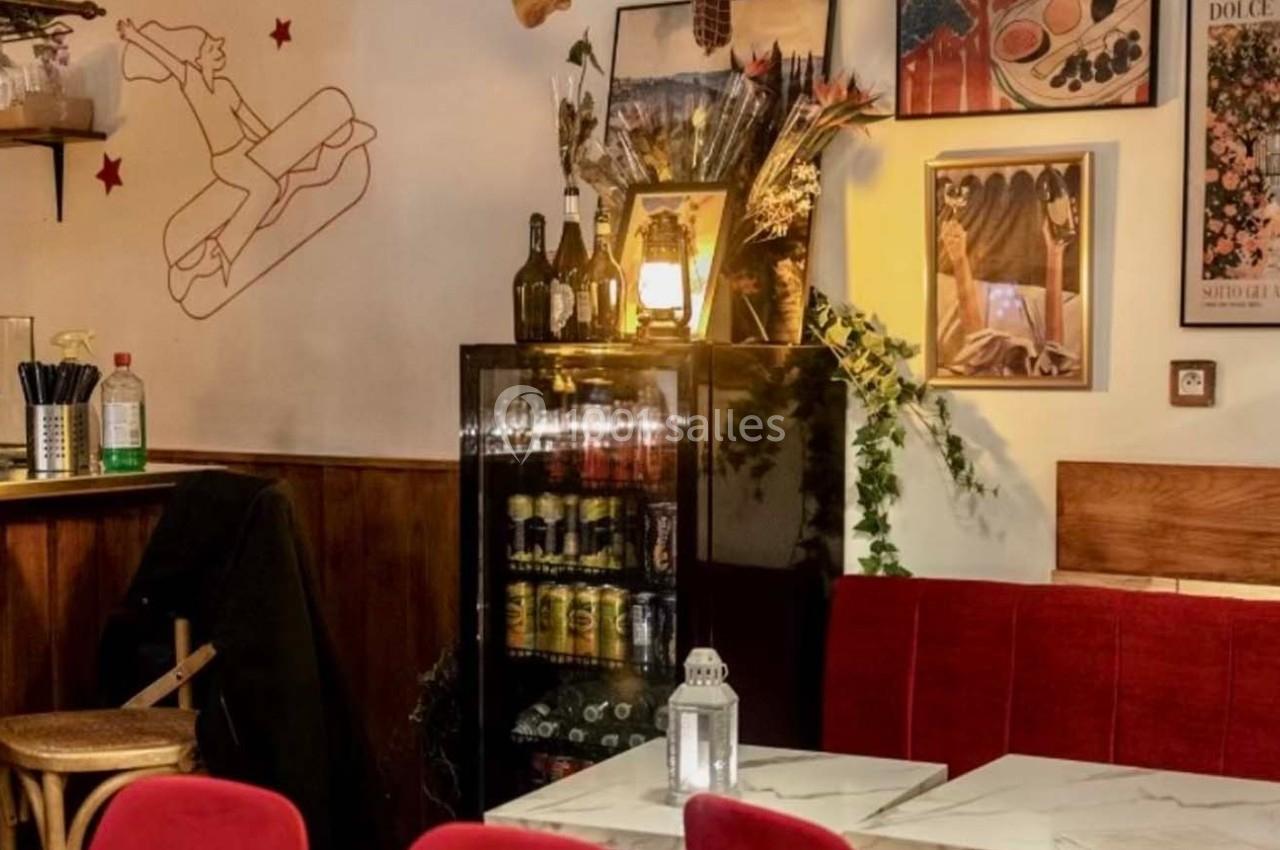 Intérieur d'un café avec banquettes rouges, table en marbre, réfrigérateur rempli de boissons et décorations murales.