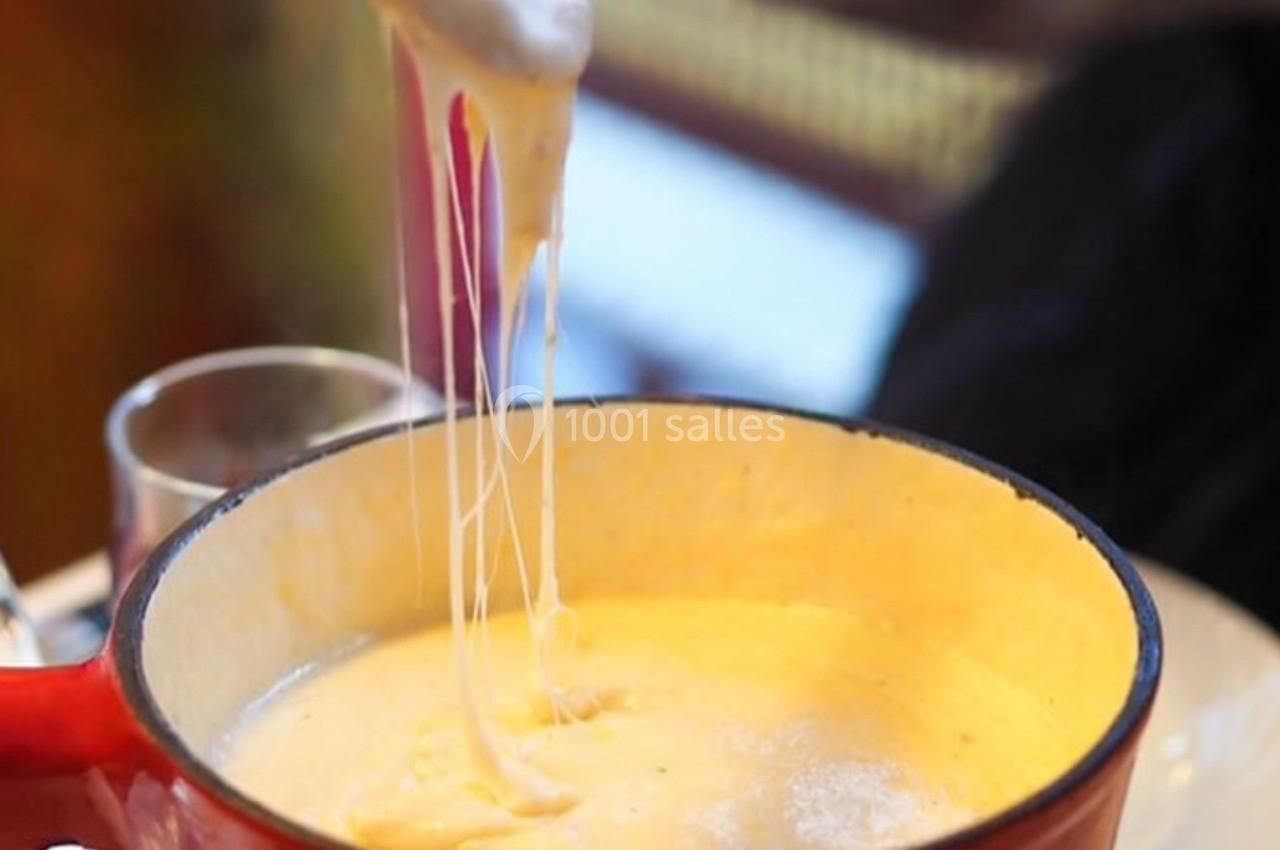 Fromage fondu filant depuis une fourchette au-dessus d'une casserole rouge remplie de fondue chaude.