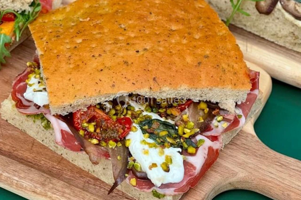 Sandwich à la focaccia garni de charcuterie, fromage frais, tomates séchées et éclats de pistaches.