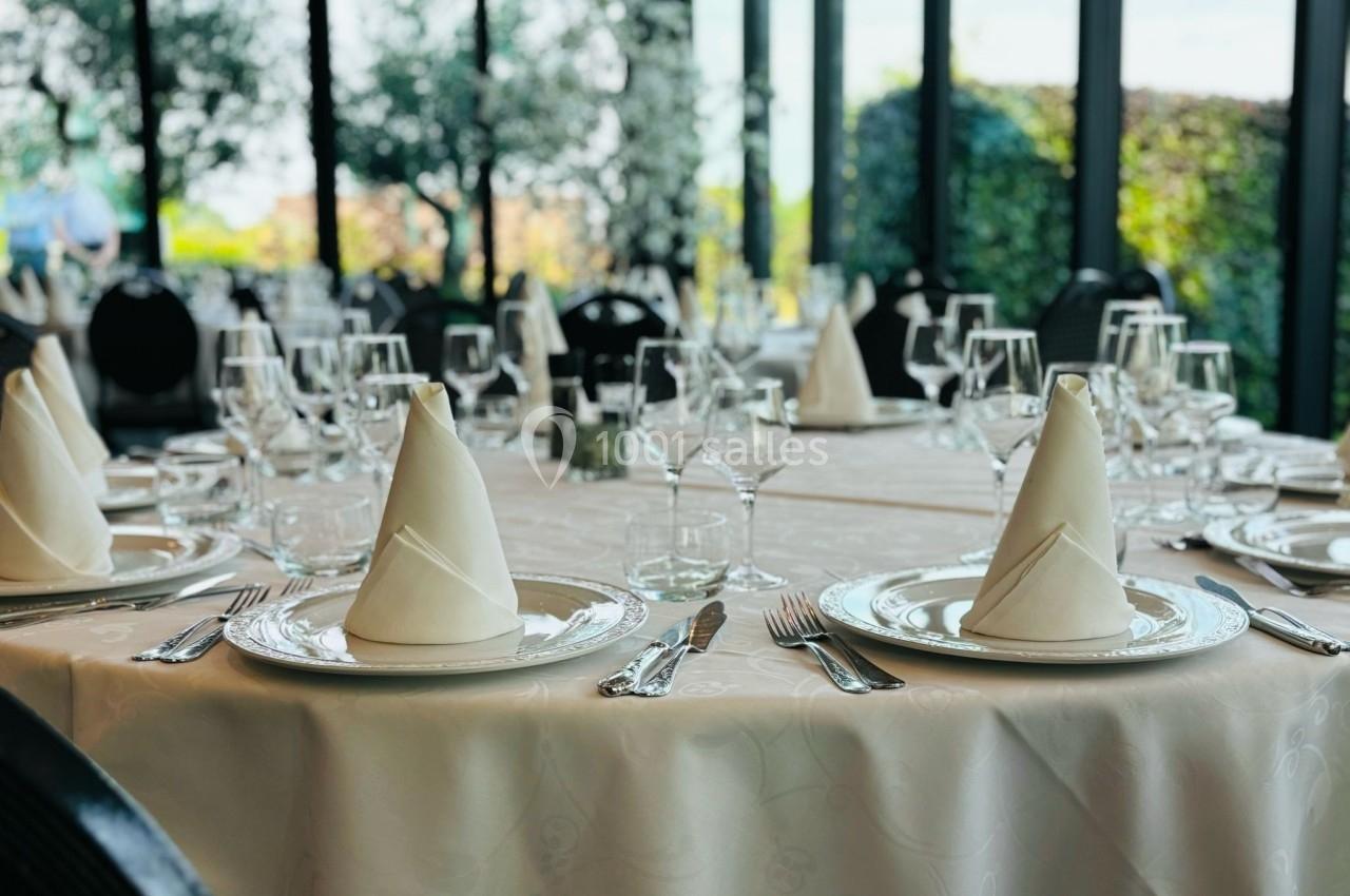 Table élégamment dressée avec nappes blanches, serviettes pliées, verres et couverts dans une salle lumineuse avec vue sur…