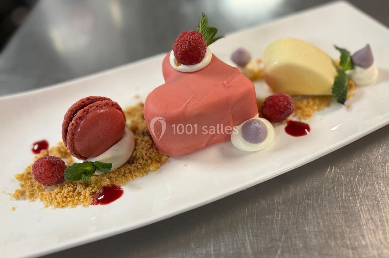 Assiette de dessert composée d'un entremets rose en forme de cœur, d'un macaron, de fruits rouges et de décorations sucrées.