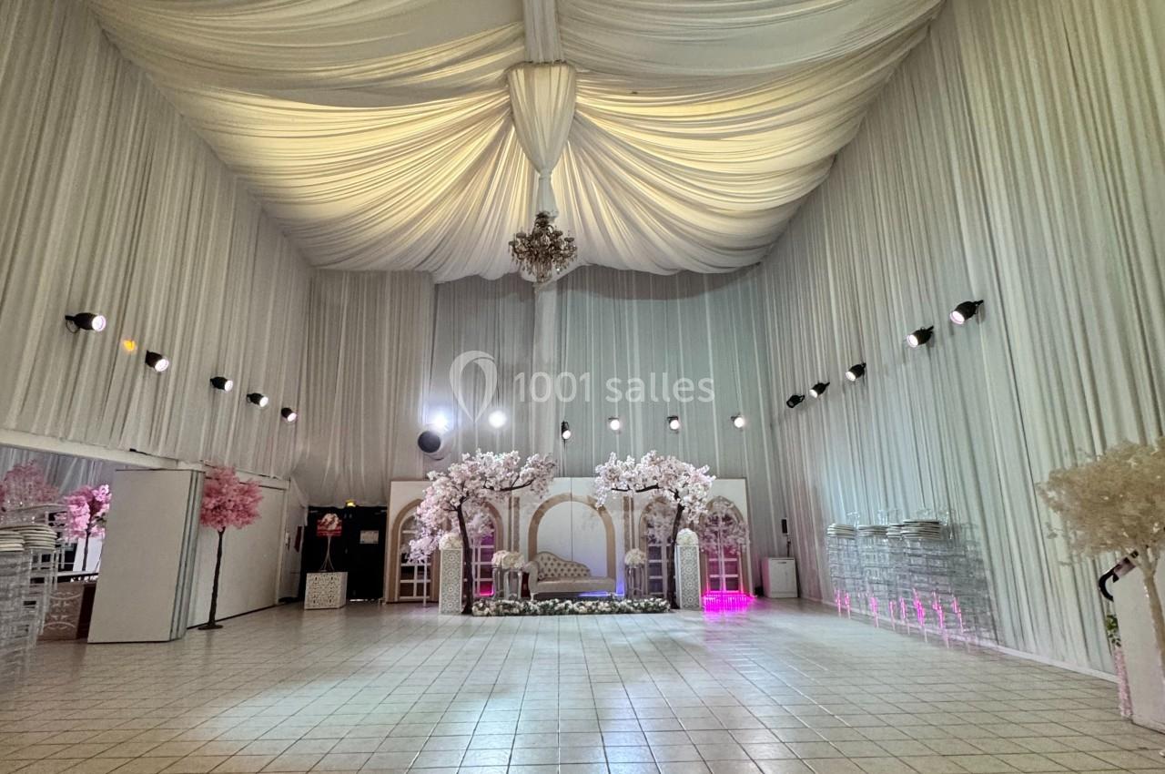 Salle de réception spacieuse avec plafond drapé, décorations florales blanches et éclairage tamisé.