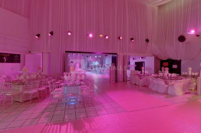 Salle de réception décorée avec des fleurs blanches, des tables élégantes et un éclairage rose tamisé.