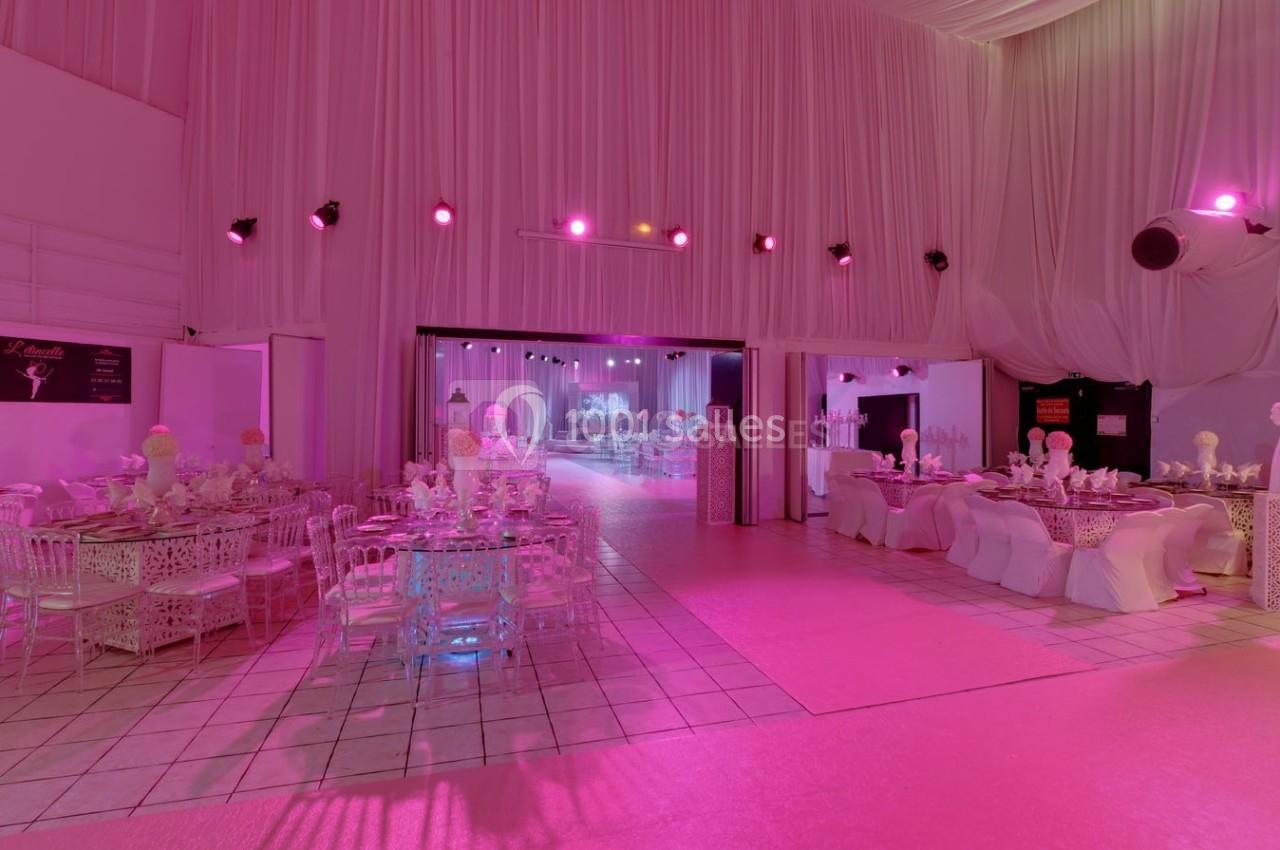 Salle de réception décorée avec des tables dressées, éclairage rose et rideaux blancs couvrant les murs.