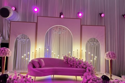 Salle de réception décorée avec des fleurs blanches, des tables élégantes et un éclairage rose tamisé.