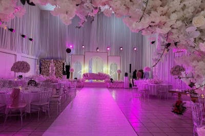 Salle de réception décorée avec des fleurs blanches, des tables élégantes et un éclairage rose tamisé.