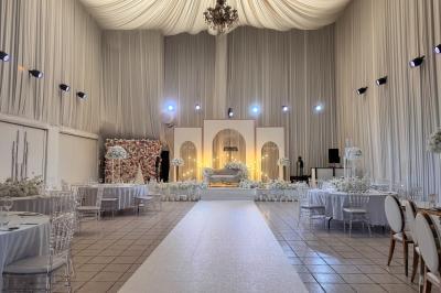 Salle de réception décorée avec des fleurs blanches, des tables élégantes et un éclairage rose tamisé.