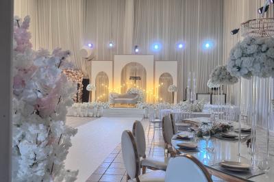 Salle de réception décorée avec des fleurs blanches, des tables élégantes et un éclairage rose tamisé.