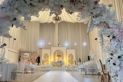 Salle de réception décorée avec des fleurs blanches, des tables élégantes et un éclairage rose tamisé.