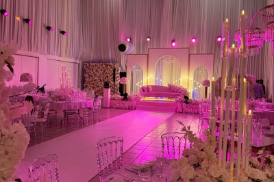 Salle de réception décorée avec des fleurs blanches, des tables élégantes et un éclairage rose tamisé.