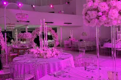 Salle de réception décorée avec des fleurs blanches, des tables élégantes et un éclairage rose tamisé.
