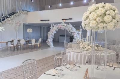 Salle de réception décorée avec des fleurs blanches, des tables élégantes et un éclairage rose tamisé.