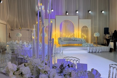 Salle de réception décorée avec des tables rondes, des chaises transparentes et des arrangements floraux blancs sous un…