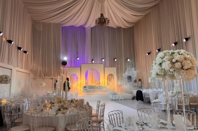 Salle de réception décorée avec des tables rondes, des chaises transparentes et des arrangements floraux blancs sous un…