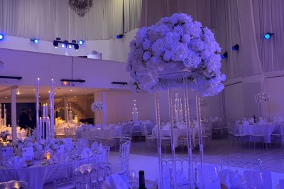 Salle de réception décorée avec des tables rondes, des chaises transparentes et des arrangements floraux blancs sous un…
