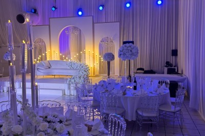 Salle de réception décorée avec des tables rondes, des chaises transparentes et des arrangements floraux blancs sous un…