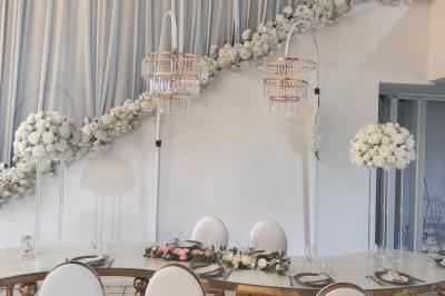 Salle de réception décorée avec des tables rondes, des chaises transparentes et des arrangements floraux blancs sous un…