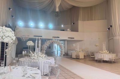 Salle de réception décorée avec des tables rondes, des chaises transparentes et des arrangements floraux blancs sous un…