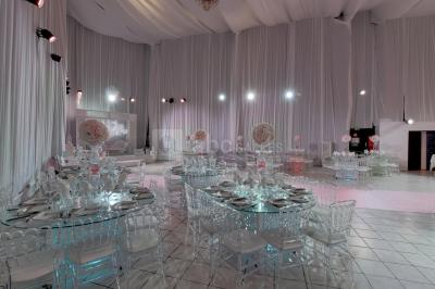 Salle de réception décorée avec des tables rondes, des chaises transparentes et des arrangements floraux blancs sous un…