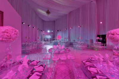 Salle de réception décorée avec des tables rondes, des chaises transparentes et des arrangements floraux blancs sous un…