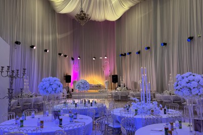 Salle de réception décorée avec des tables rondes, des chaises transparentes et des arrangements floraux blancs sous un…