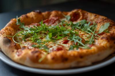 Une pâte à pizza soulevée pour montrer son élasticité, avec une garniture de sauce tomate et fromage visible.