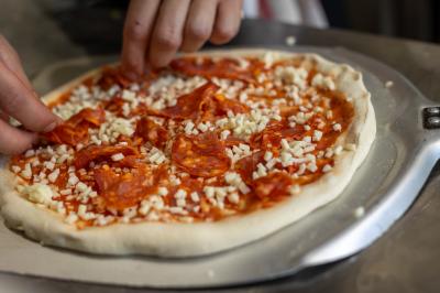 Une pâte à pizza soulevée pour montrer son élasticité, avec une garniture de sauce tomate et fromage visible.