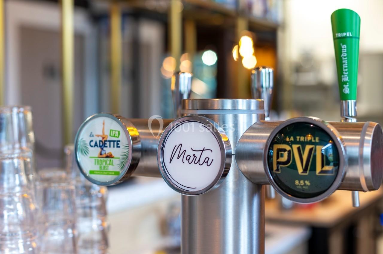 Tireuse à bière avec trois robinets affichant les marques ’La Cadette’, ’Marta’ et ’PVL’, dans un bar lumineux.