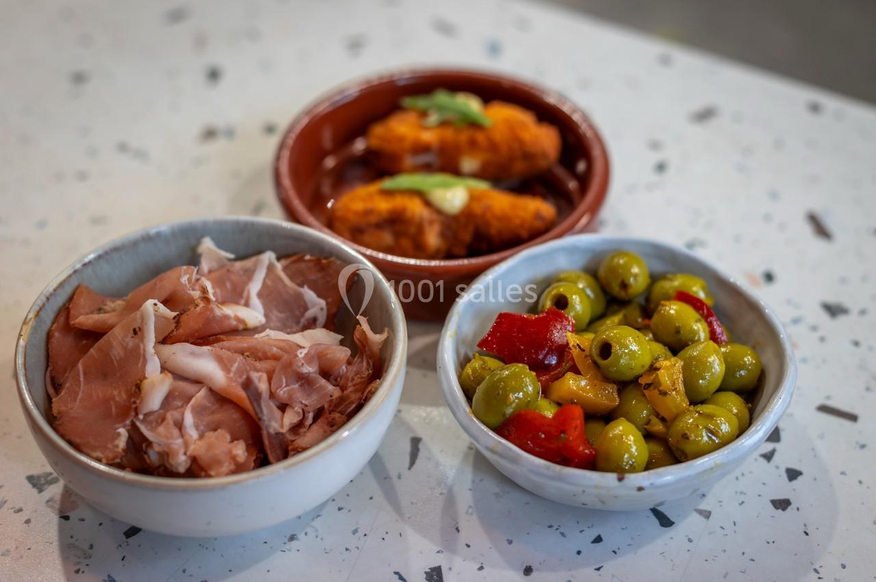 Assortiment de tapas comprenant du jambon cru, des olives marinées et des croquettes servies dans des bols.