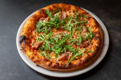 Préparation d'une pizza avec des mains ajoutant des tranches de chorizo sur une pâte garnie de sauce tomate et fromage râpé.