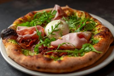 Préparation d'une pizza avec des mains ajoutant des tranches de chorizo sur une pâte garnie de sauce tomate et fromage râpé.