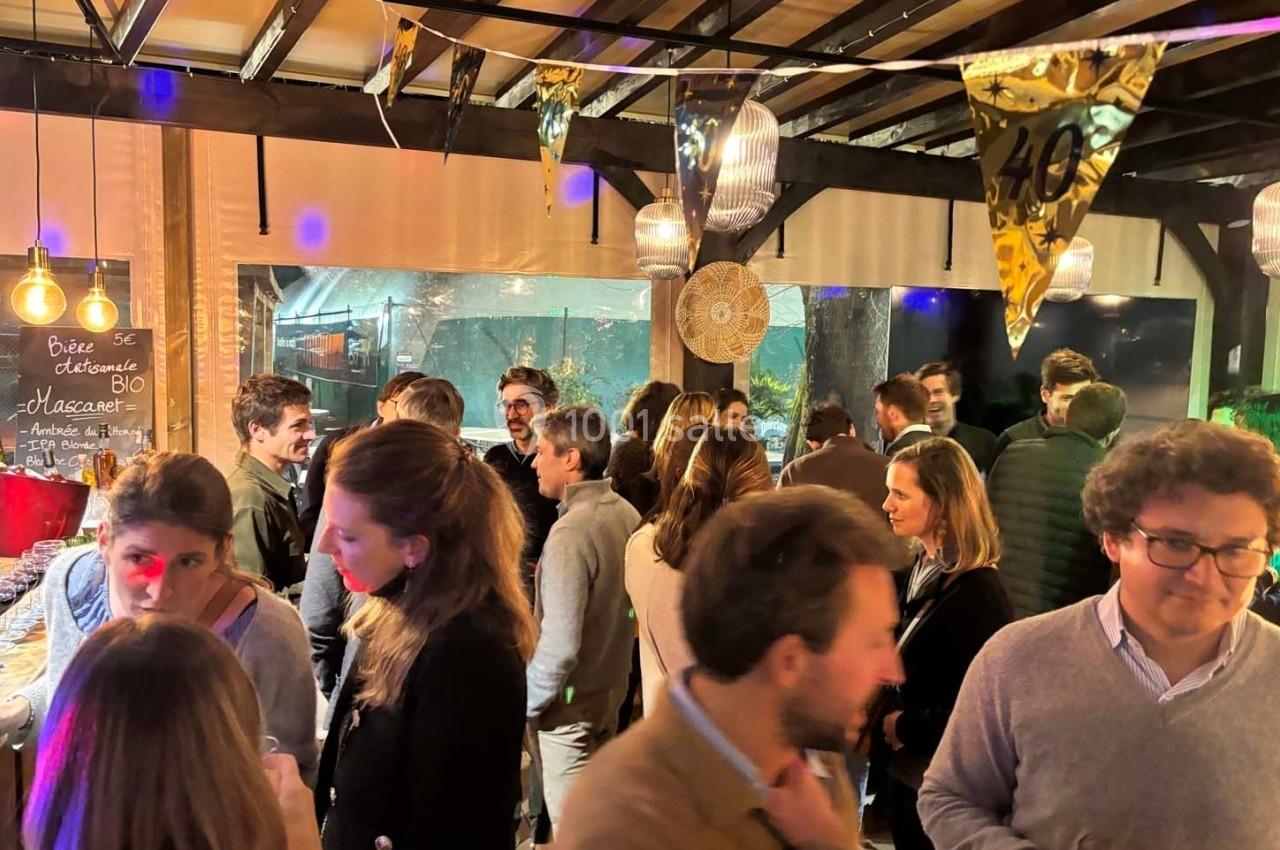 Groupe de personnes discutant dans un espace intérieur décoré pour une fête, avec des guirlandes et un panneau lumineux.