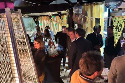 Entrée d'un café avec une grande terrasse, un parasol orange et des meubles en osier sous un ciel bleu.