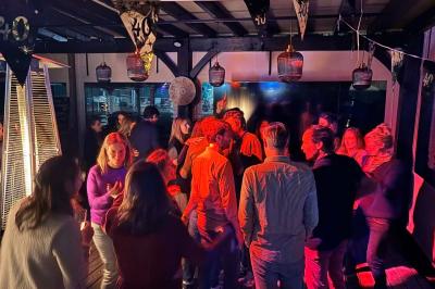 Entrée d'un café avec une grande terrasse, un parasol orange et des meubles en osier sous un ciel bleu.