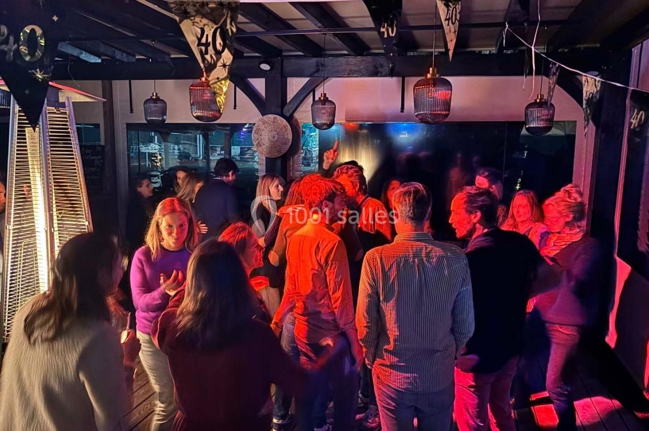 Groupe de personnes dansant et discutant sous des lumières colorées lors d'une fête en intérieur.