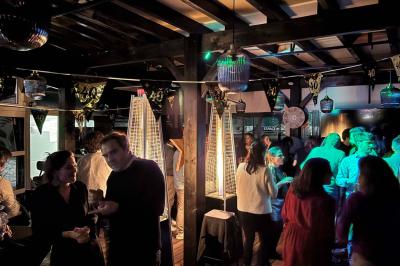 Entrée d'un café avec une grande terrasse, un parasol orange et des meubles en osier sous un ciel bleu.
