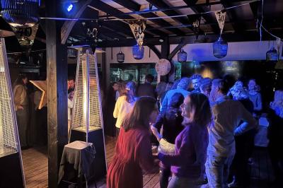 Entrée d'un café avec une grande terrasse, un parasol orange et des meubles en osier sous un ciel bleu.