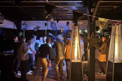 Entrée d'un café avec une grande terrasse, un parasol orange et des meubles en osier sous un ciel bleu.