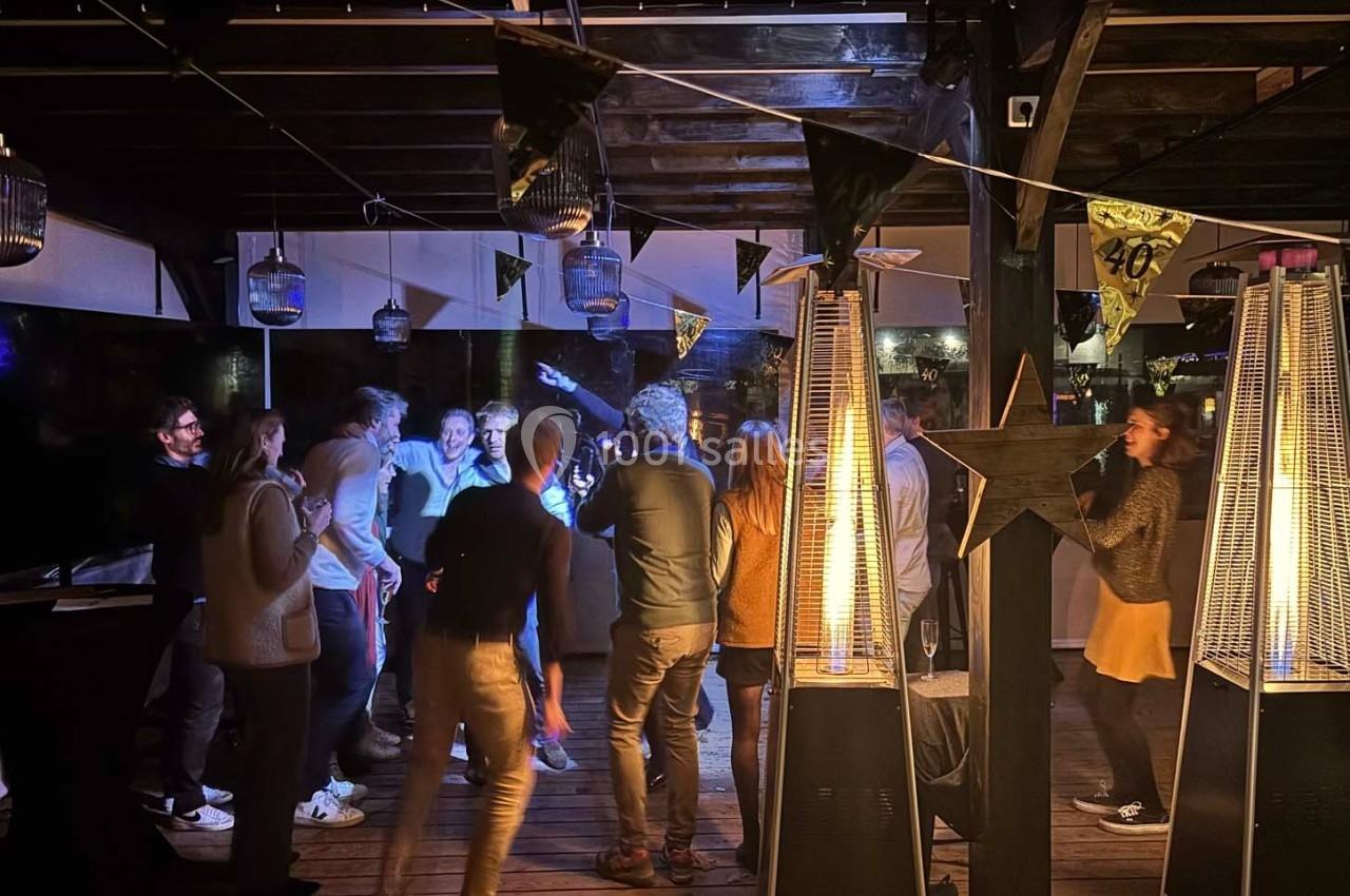 Groupe de personnes dansant et discutant lors d'une soirée festive en extérieur, éclairée par des lampes chauffantes.