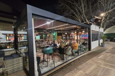 Entrée d'un café avec une grande terrasse, un parasol orange et des meubles en osier sous un ciel bleu.