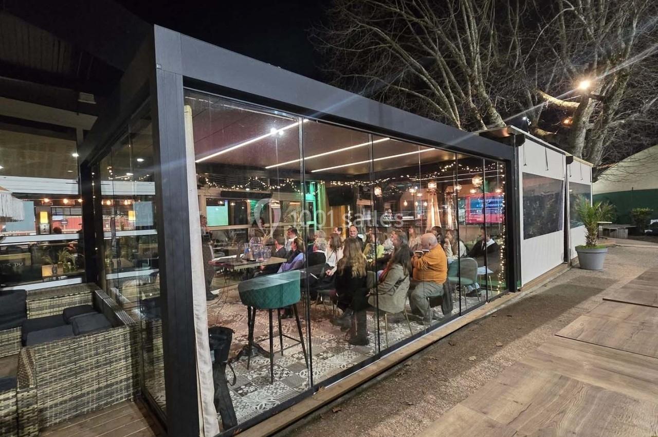 Un groupe de personnes dînant à l'intérieur d'une terrasse vitrée éclairée, entourée d'arbres en soirée.
