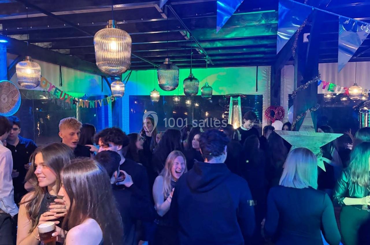 Des personnes dansent et discutent lors d'une soirée festive, éclairée par des lumières colorées et des décorations…